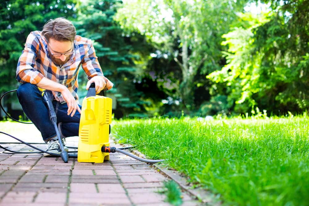 A young man works in the garden using a yellow compact home high pressure washer