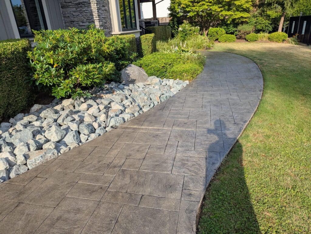 Freshly sealed stamped concrete walkway running alongside a landscaped garden bed